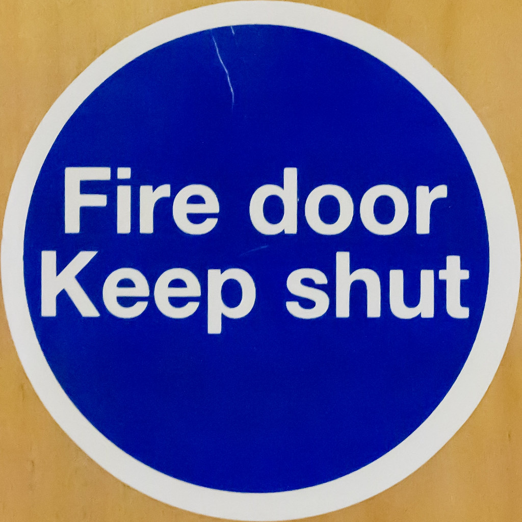 Blue 'Fire door, keep shut' safety sign fixed to a timber fire door.